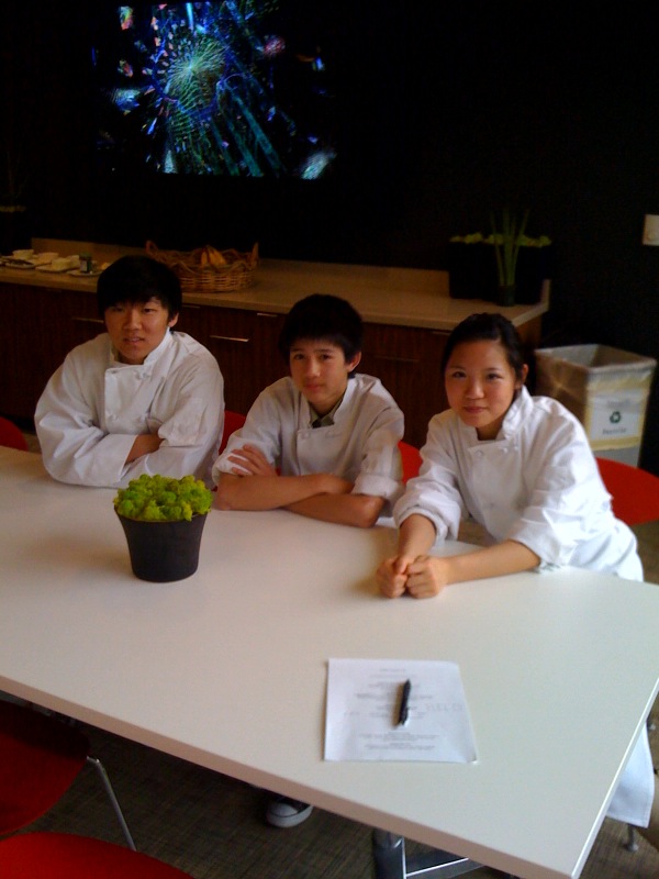 2 students taking a photograph with a chef. All are wearing cooking attire.